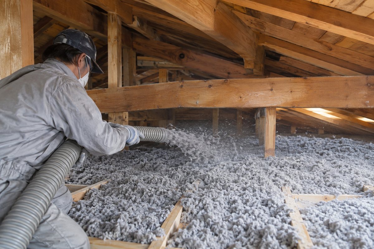 小屋裏で職人がホースから天井の上にセルロースファイバーを吹き込む断熱リフォーム