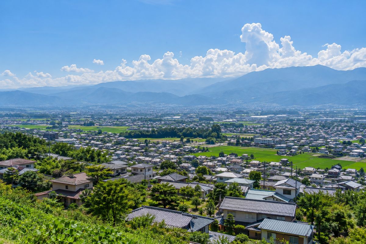 夏の盆地のまちと、遠くの山並みの上に立つ入道雲